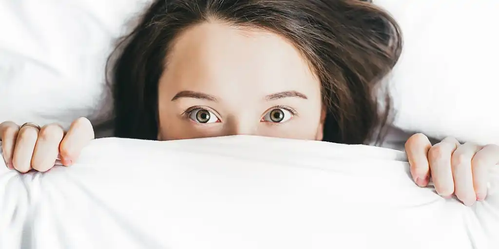 Female hiding underneath bed covers covering her face