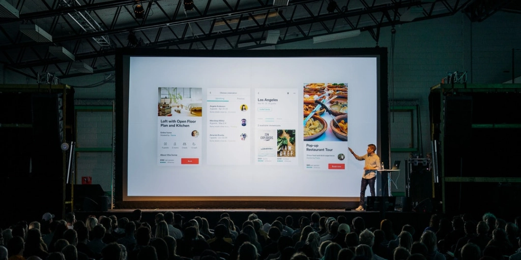 man presenting UI of app on large screen at conference