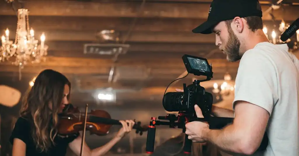 Man working videography as side hustle, filming woman playing violin