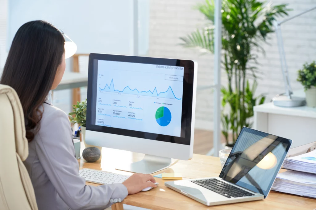 Woman looking at Google Analytics data on desktop monitor and laptop.