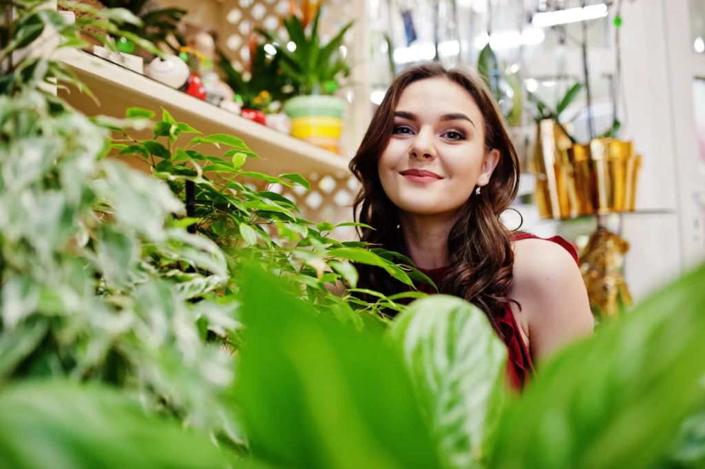 Woman smiling surrounded by green plants in a garden shop.