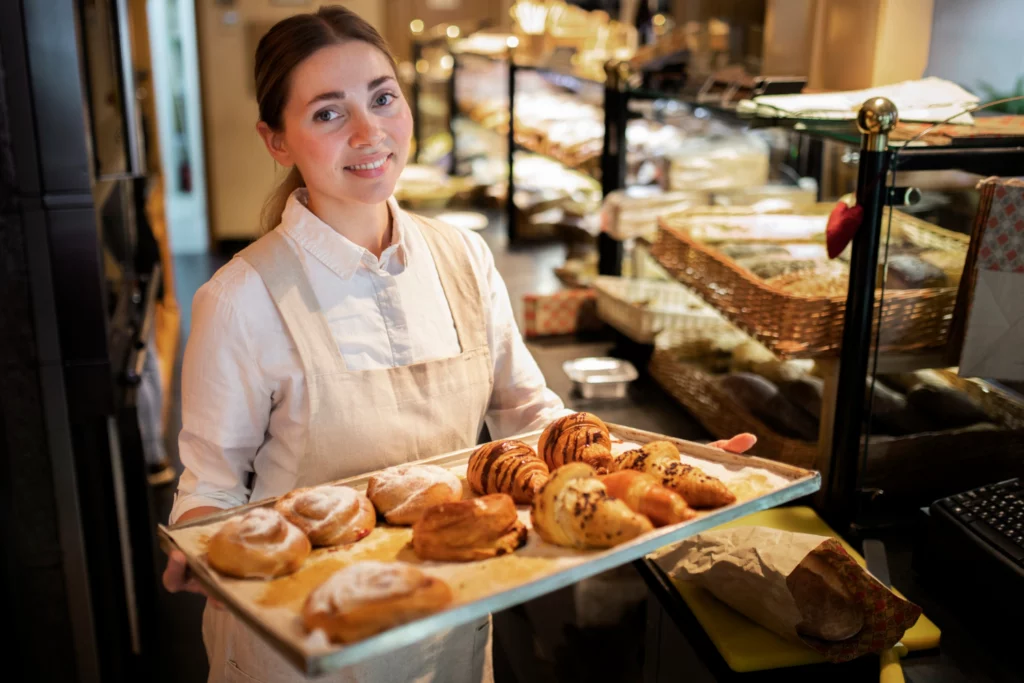 Woman running bakery - holding tray of fresh pastries.