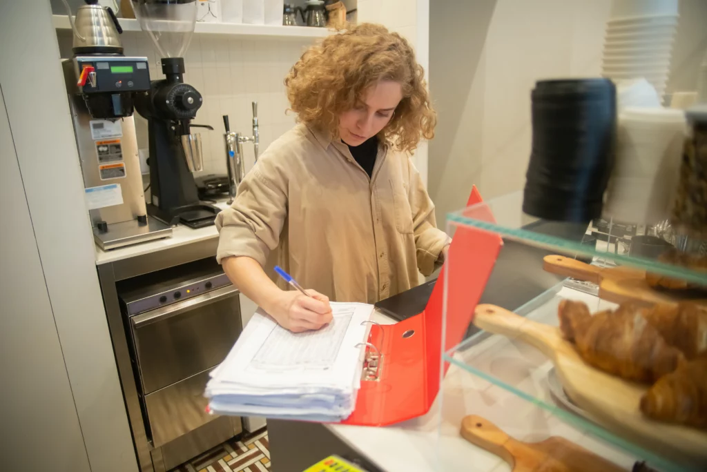 Bakery owner looking in notebook. She’s managing her inventory by recording the number of pastries for sale.