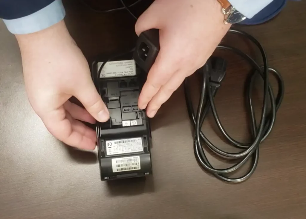 Screenshot of man showing the back for the Dejavoo Z11 credit card machine. He’s showing where to plug in the power cord on the back of the device.