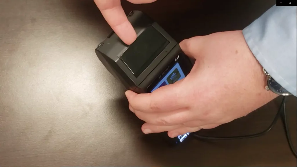 Man showing how to replace terminal receipt paper with the Dejavoo Z11 credit card machine. At the top of the device, just past the card tap, is a small lip. Place your finger there, and flip up until you hear a small click.