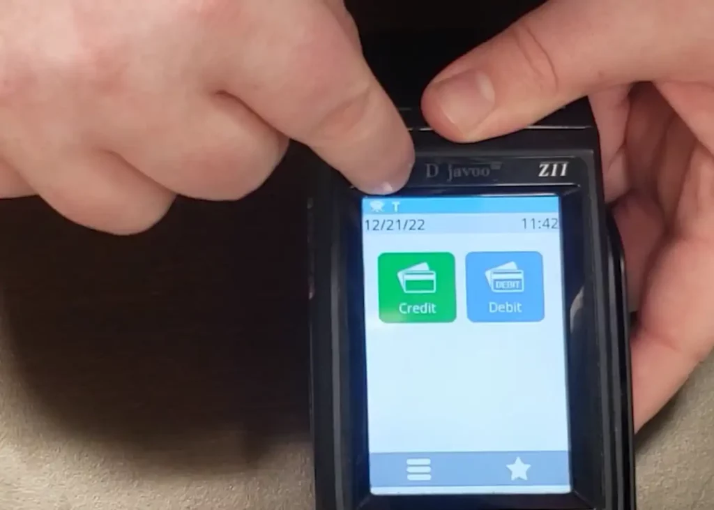 Man holding the Dejavoo Z11 terminal shows that in training mode, there is a small letter “T” in the top left corner of the touchscreen.