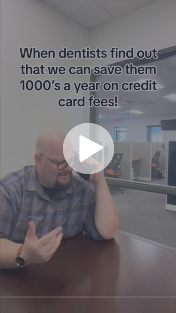 A screengrab shows the play button at the center, black text at the top saying when dentists find out that we can save them 1000’s a year on credit card fees! Man with glasses wearing a wristwatch and plaid shirt is holding a cellphone to his ear